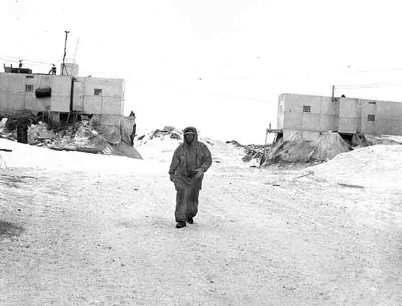 Crew member of Drift Station Alpha in the Arctic Ocean walks along the ice floe, with a building visible in the background