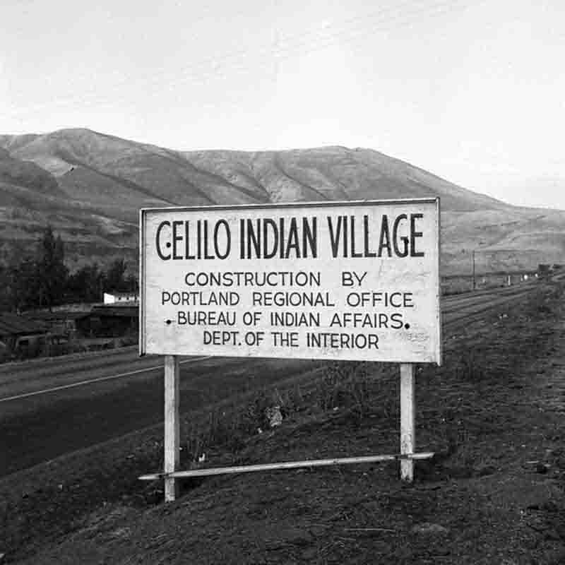 This 1956 photograph by Peter Bock-Schroeder captures a significant moment of upheaval for the Indigenous communities of the Columbia River. The sign prominently displays the involvement of the Bureau of Indian Affairs (BIA) in the construction of a new 'Celilo Indian Village,' a project necessitated by the imminent completion of The Dalles Dam.