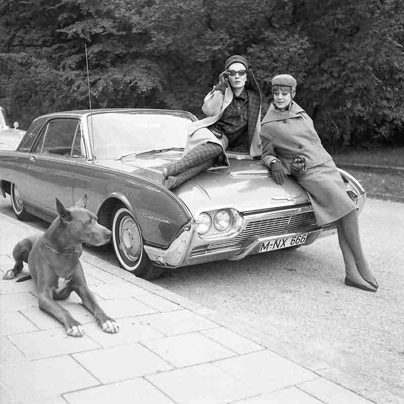 Models sitting on a car with a Doberman in the foreground 
