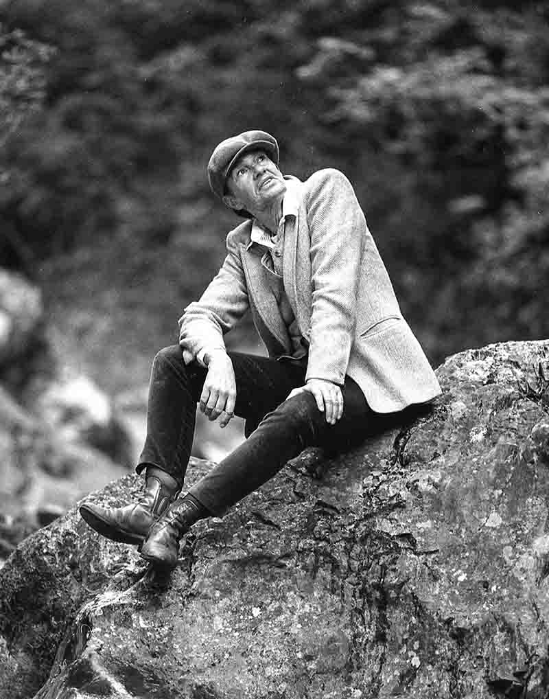 A female model dressed as a man sits on a rock in a Bavarian mountain gorge