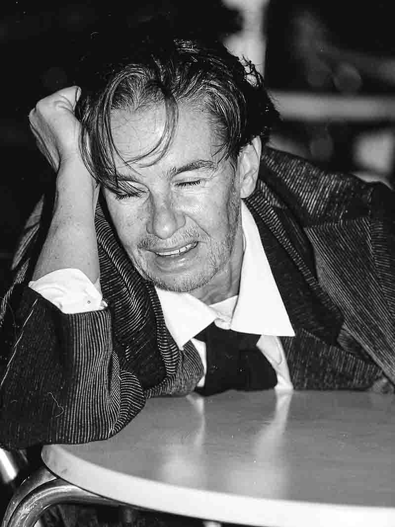 A female model disguised as a male sits at a bistro table