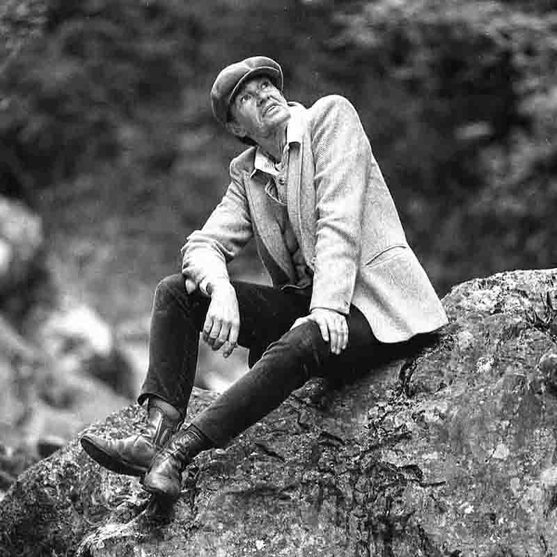 A female model dressed as a man sits on a rock in a Bavarian mountain gorge