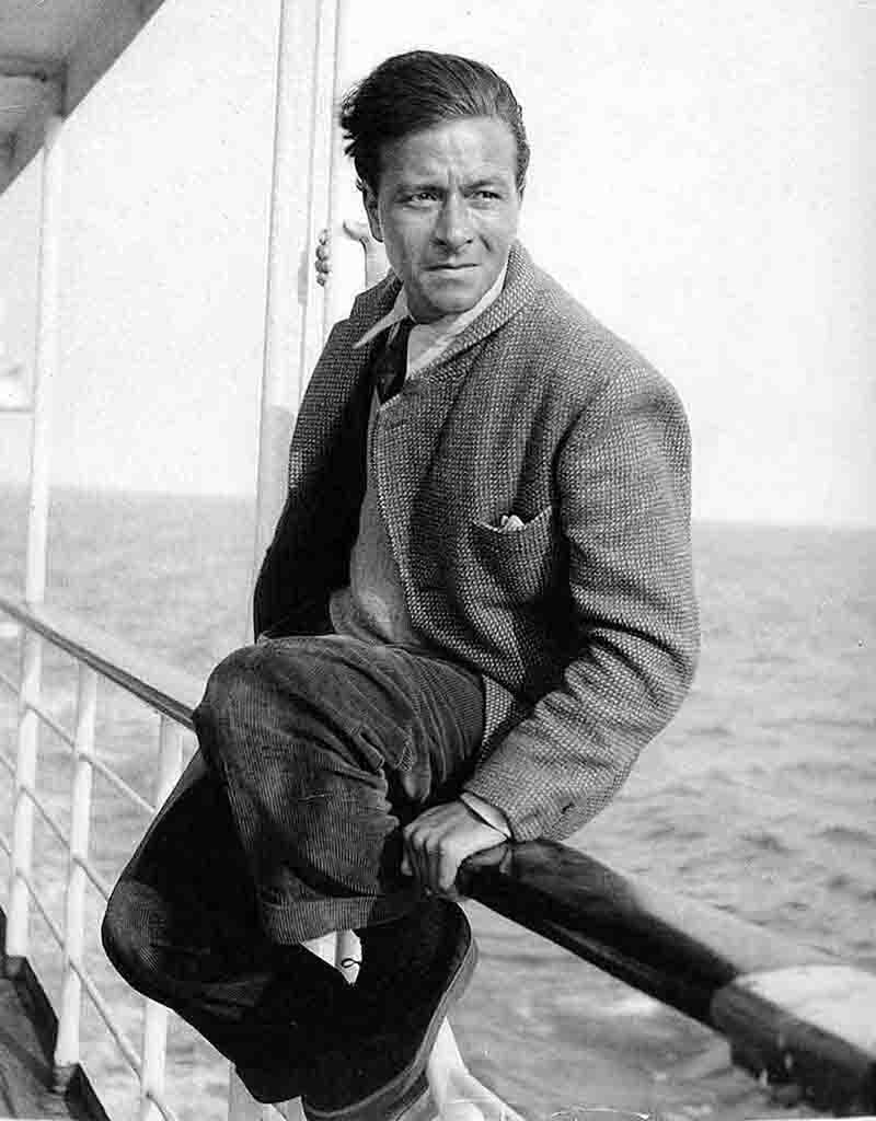 A black and white portrait of German photojournalist Peter Bock-Schroeder (1913–2001) sitting on the railing of a ship at sea.