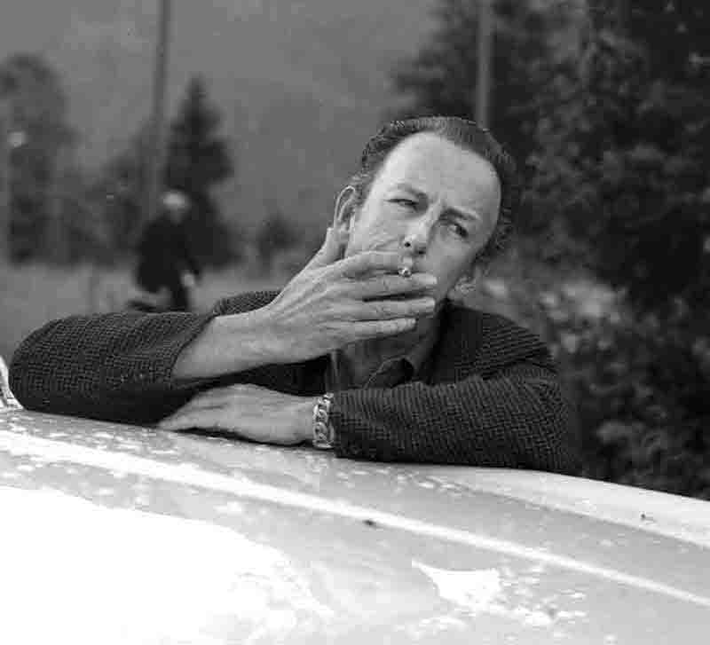 Count Albrecht von Goertz casually leaning on a car and smoking a cigarette.