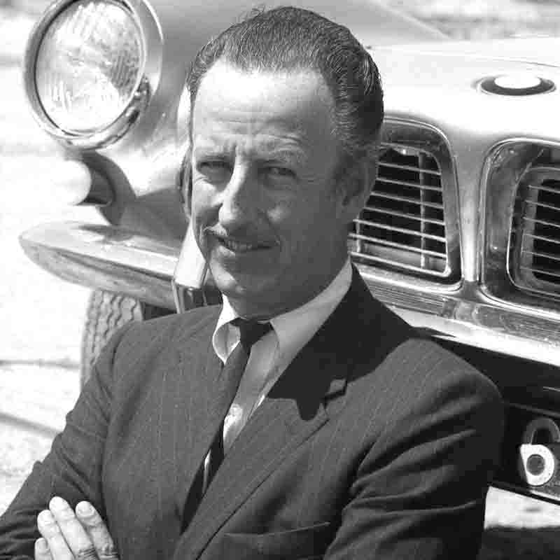 A well-dressed man, Graf Goertz,  standing beside a BMW 507 car, exuding professionalism and elegance.