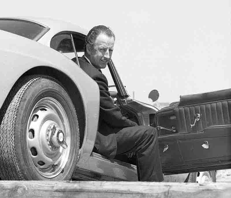 A man in a suit sitting in the open door of a BMW 507 sports car.