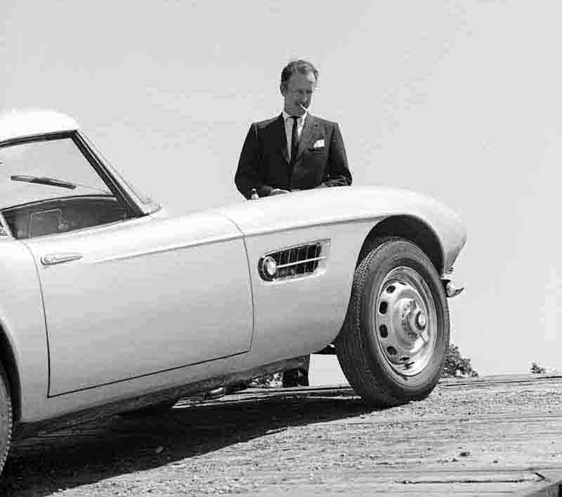 A stylish man in a tailored suit standing confidently next to a sleek sports car.