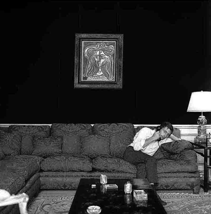 Gunter Sachs with Bust of a woman by Pablo Picasso Gunther Sachs on the phone reclines on a couch in a cozy living room, surrounded by warm lighting and decorative elements.