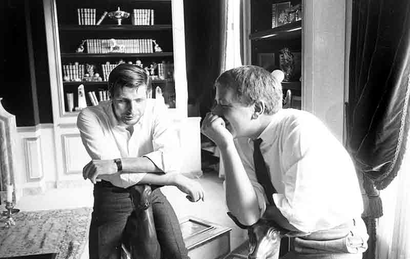 Gunter Sachs and Peter Bock-Schroeder, two men seated in a room filled with bookshelves, engaged in conversation.