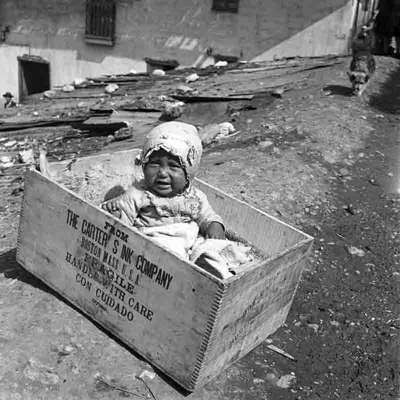 Indigenous baby in Peru sitting in a wooden box labeled - Handle with care.