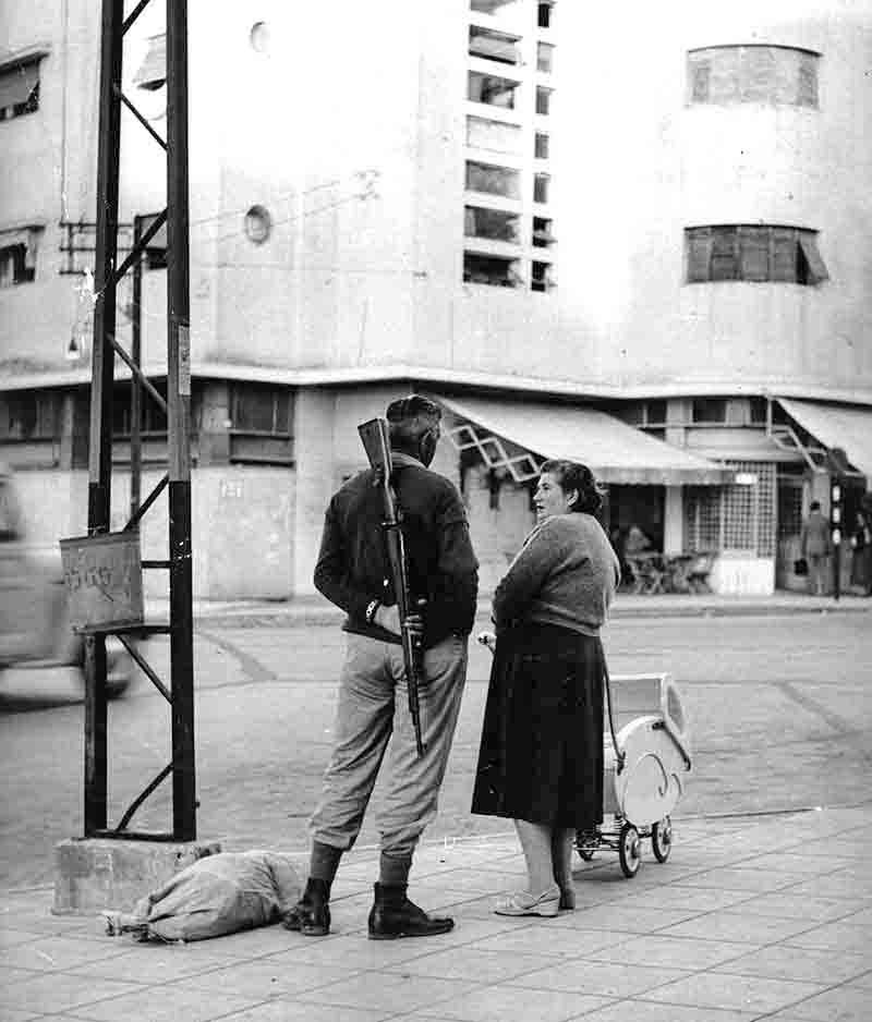 Man with rifle part of Israeli civil defence during Suez crisis talking to a woman
