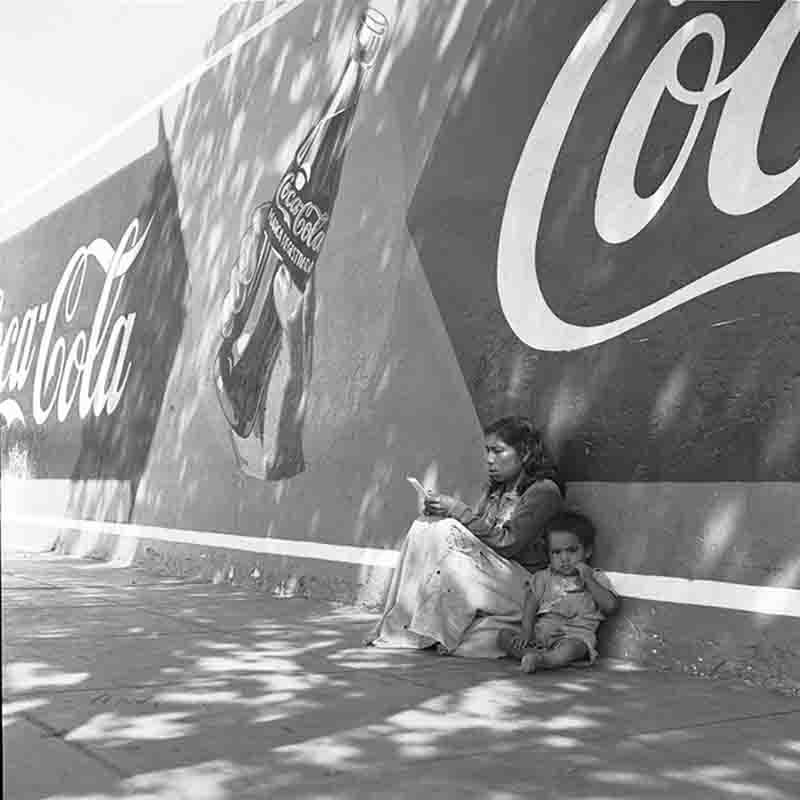 Indigenous mother with her child sitting on a sidewalk in Peru's capital Lima in front of a Coca Cola advertisement
