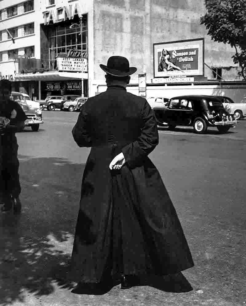 Priest crossing a street in Lima, Peru. On the opposite side is a billboard advertising the biblical film Samson and Delhiha.