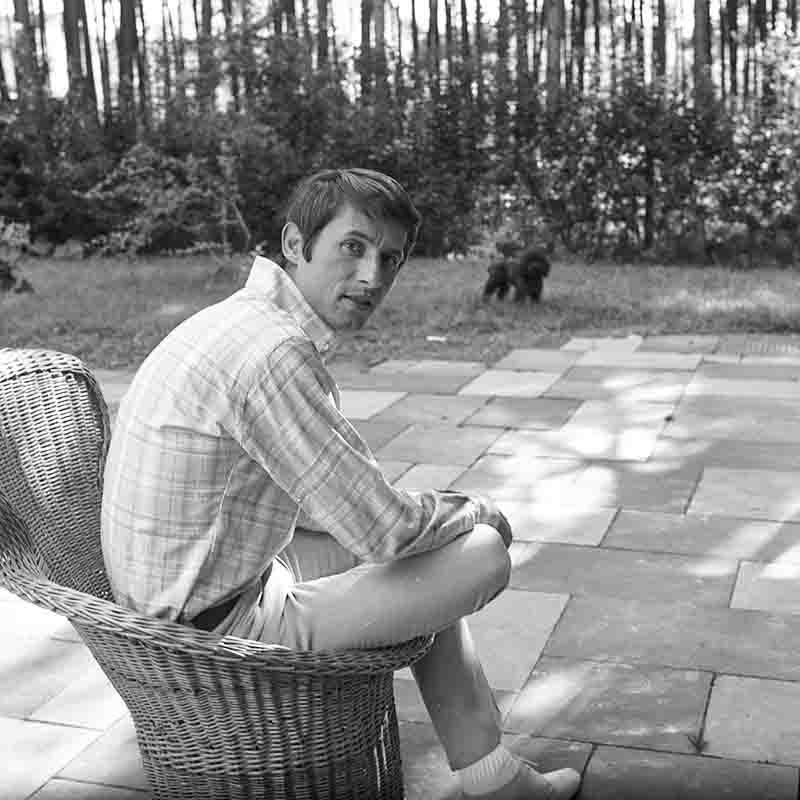 Pop singer Udo Jürgens relaxes in a wicker chair, enjoying the company of a dog by his side.